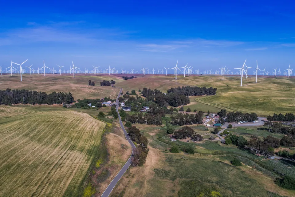 Aerial view of small community among green agricultural fields and wind turbines in Solano County, Northern California.